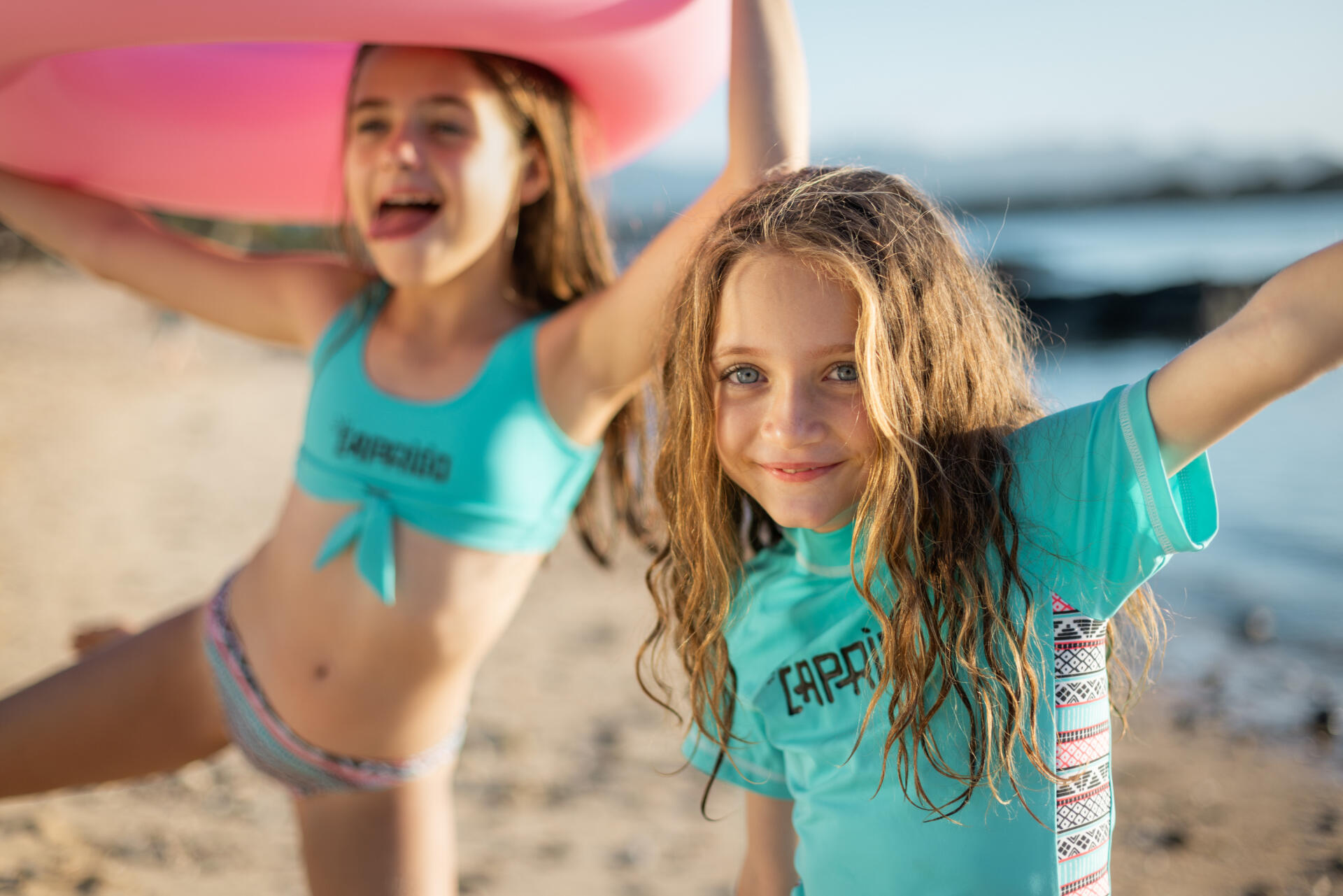 Two children in swimsuits, one child holding a pink swimming ring in their hand.