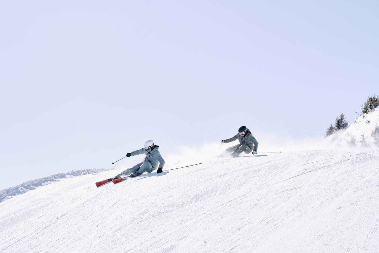 Two skiers skiing down the slope under a blue sky
