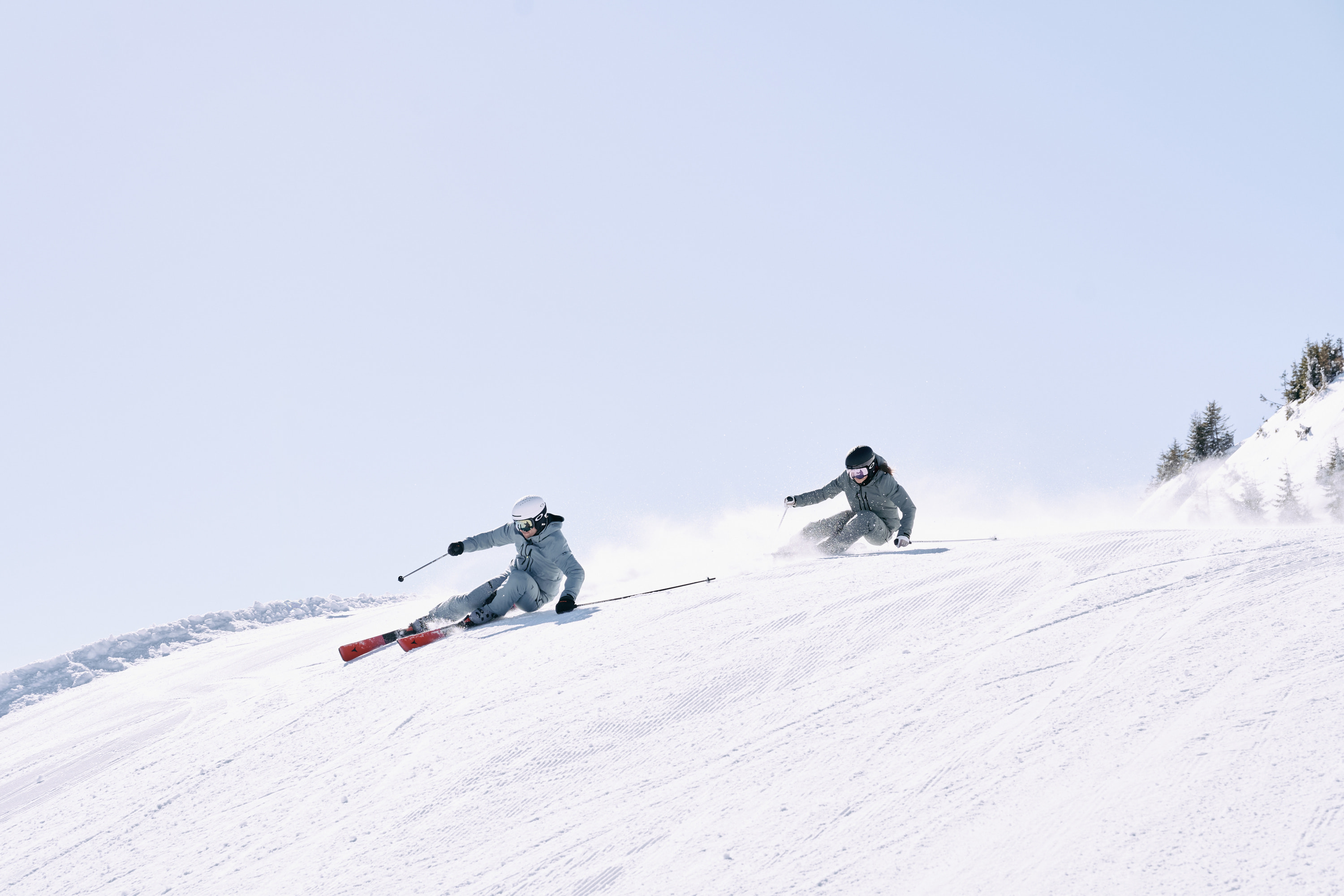 Two skiers skiing down the slope under a blue sky
