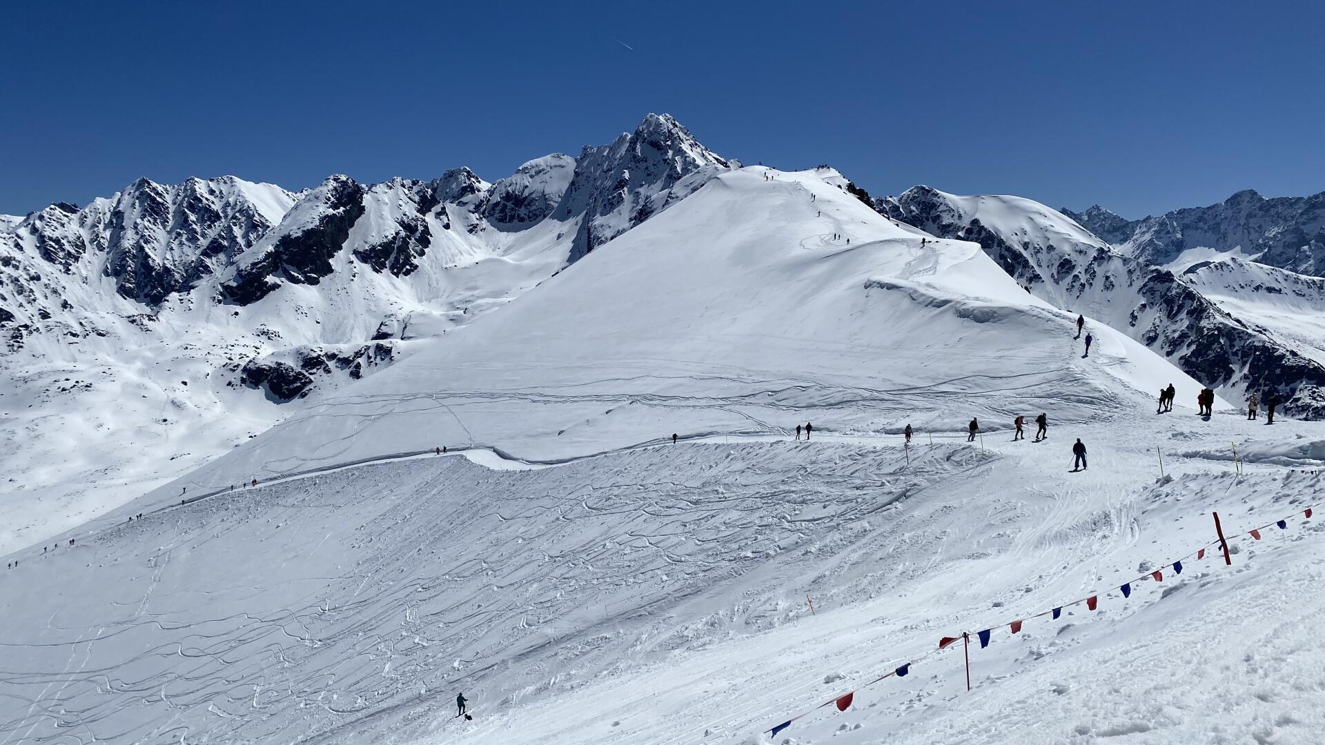Verschneite Berge am Tag, Skifahrer fahren auf einer Bergpiste entlang.