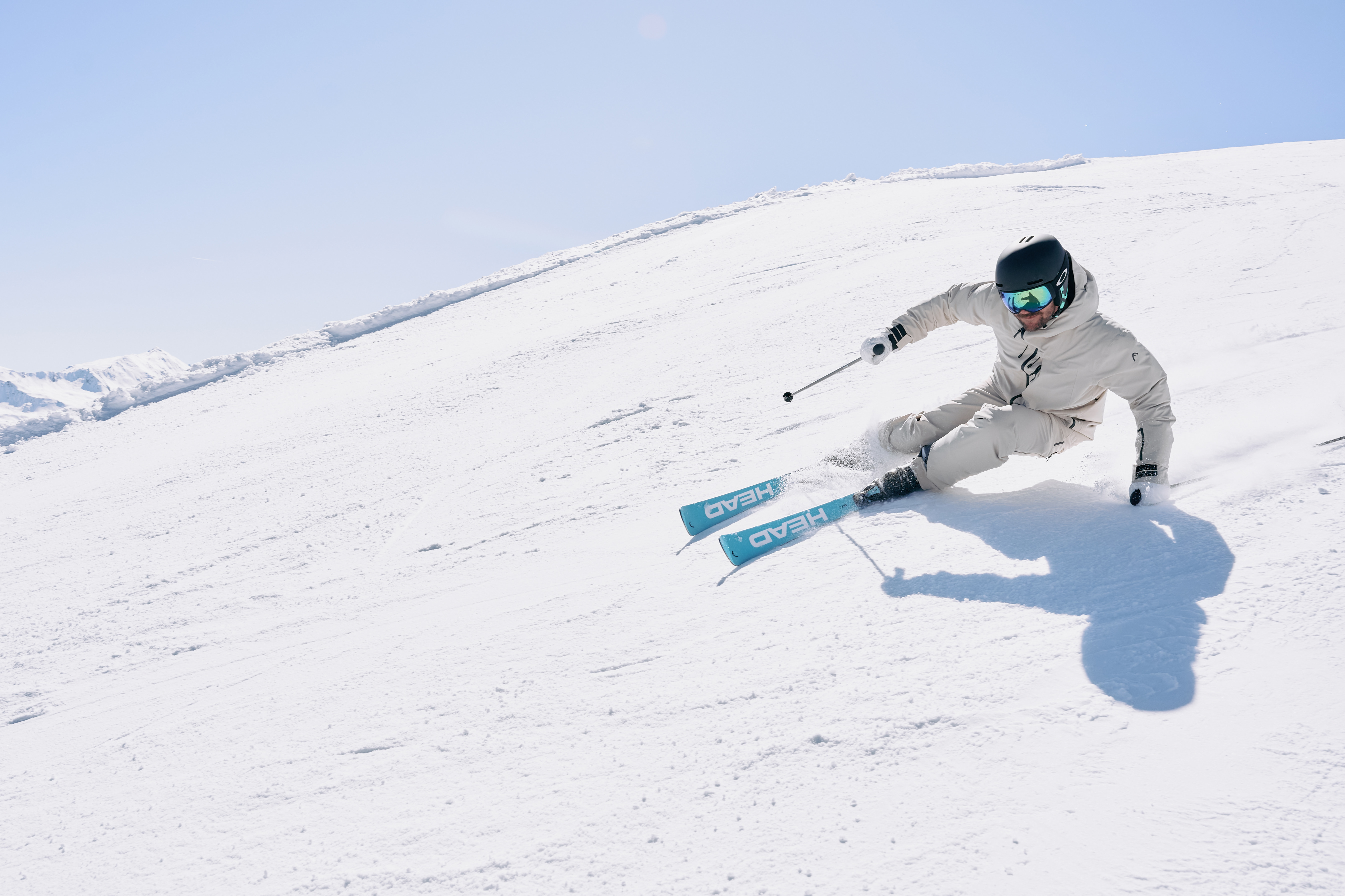 Skifahrer in weißem Anzug, der an einem strahlenden Sonnentag einen verschneiten Berghang hinunterfährt. Wintersport.