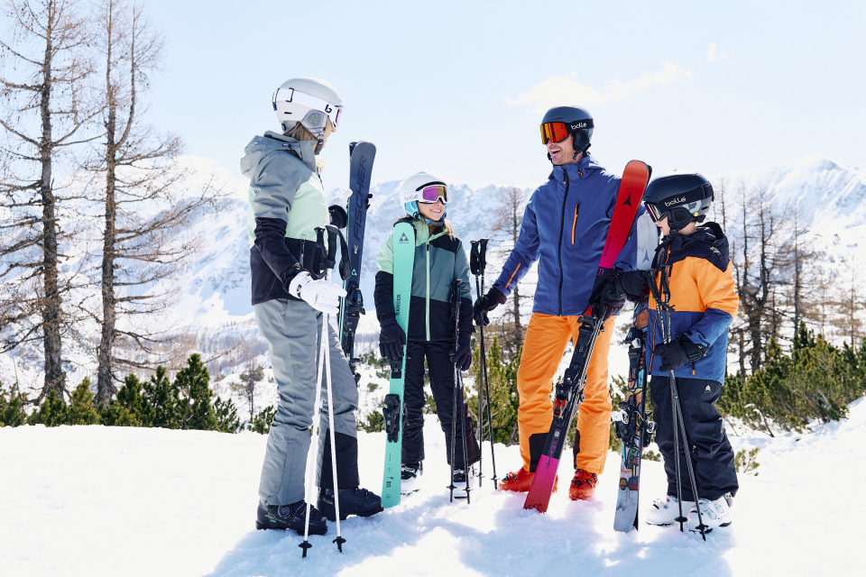 The parents are standing in the snow with their two children and smiling at each other.