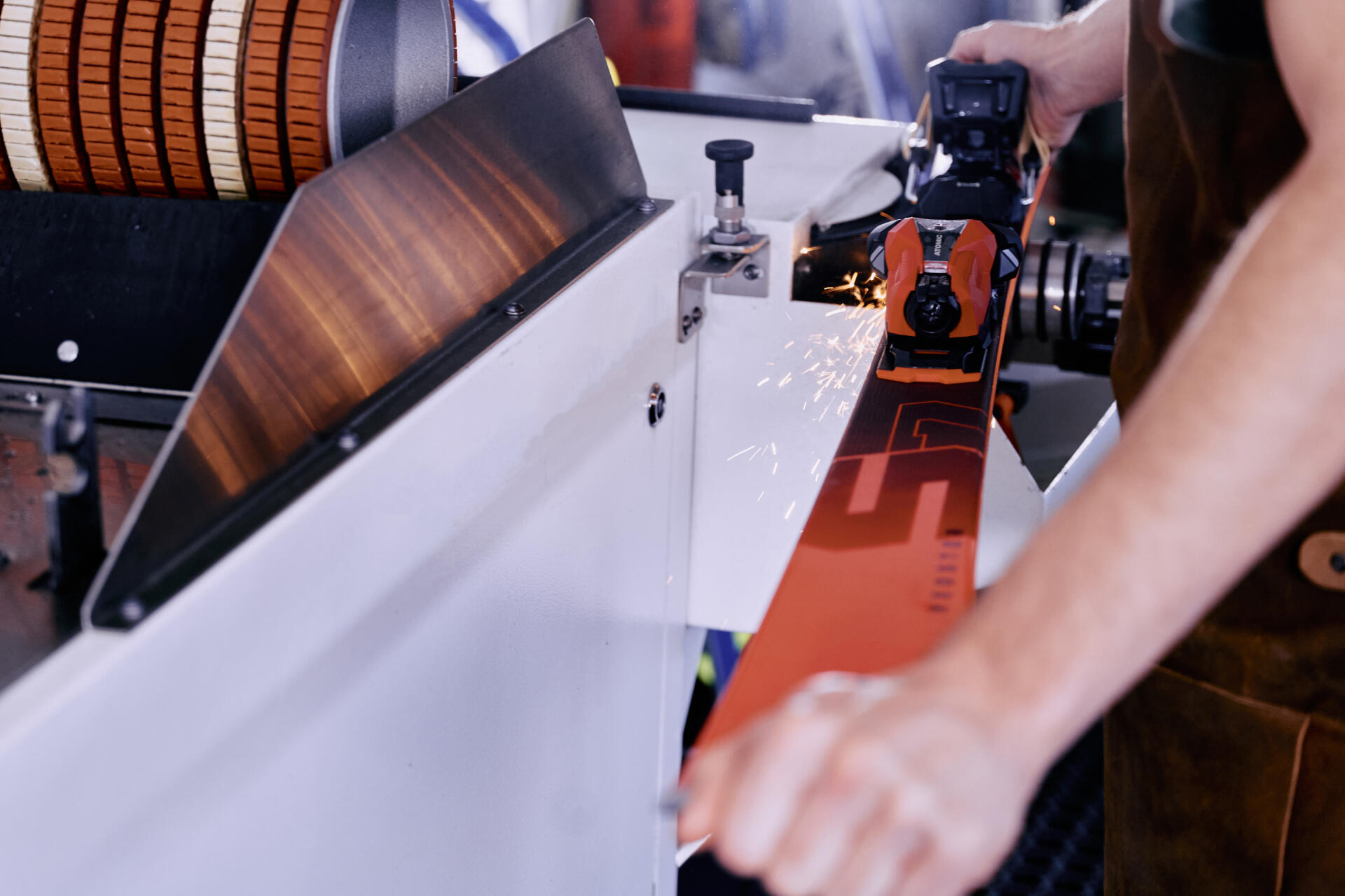 A person sharpens a ski on a grinding machine, causing sparks to fly.