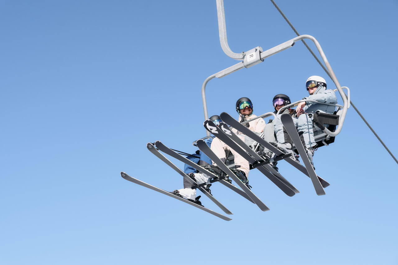 Four skiers are sitting on the chairlift and riding up the mountain.