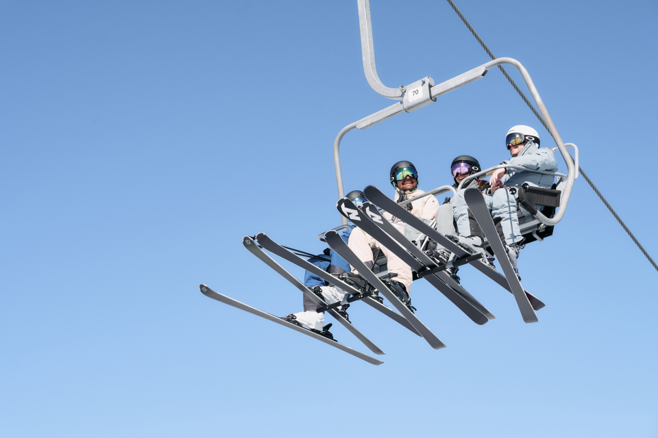 4 Skifahrer sitzen auf dem Sessellift und fahren den Berg hinauf