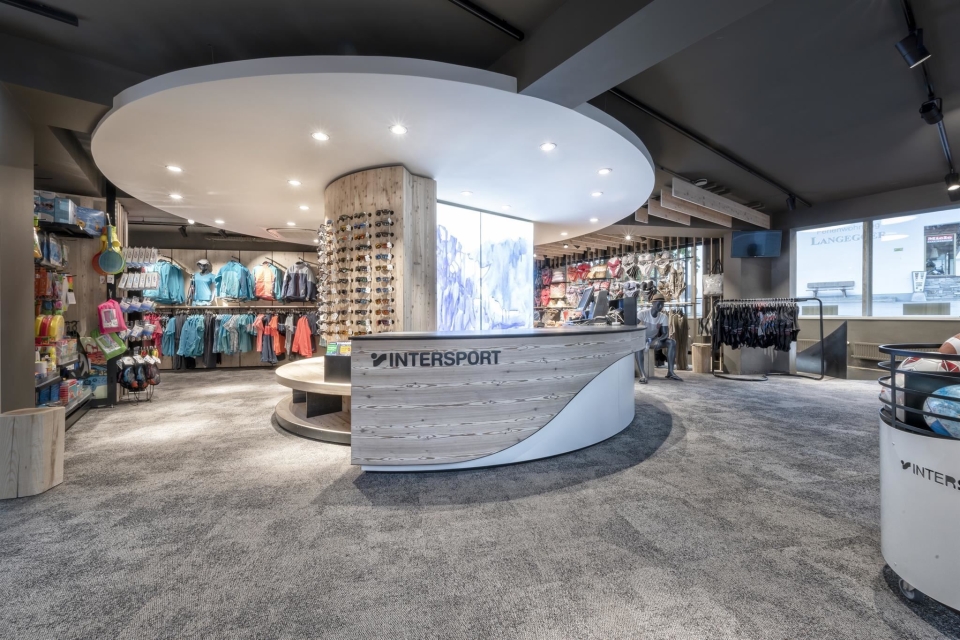 Innenraum eines Intersport-Geschäfts mit ausgestellten Jacken, Sonnenbrillen und weiterer Ausrüstung für Ski- und Radsport.