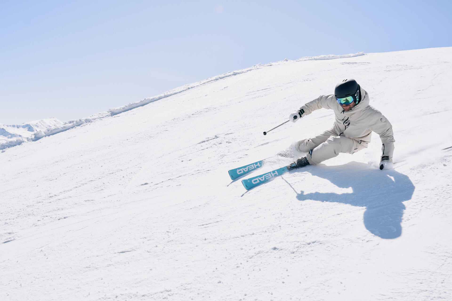 Ein Skifahrer mit heller Bekleidung und türkisen Ski fährt die Piste hinunter